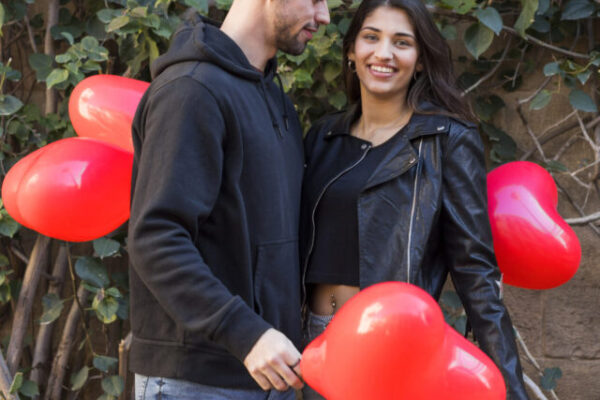 young-guy-near-smiling-lady-holding-balloons-form-hearts